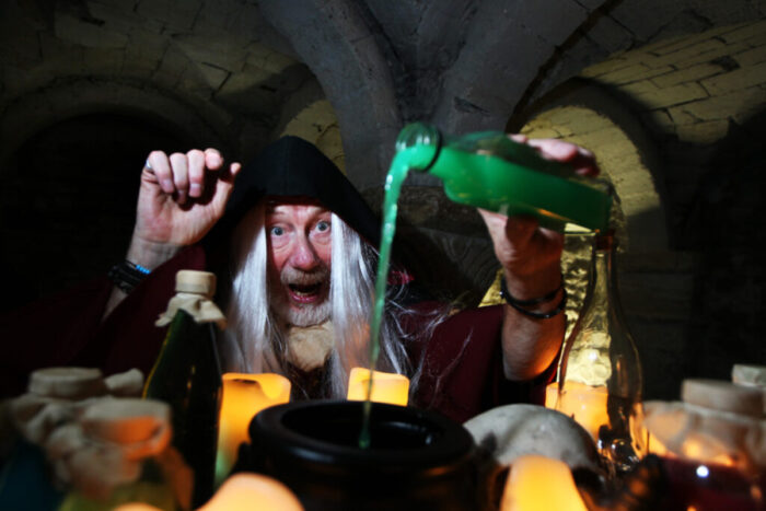 Merlin the Wizard pouring a green elixir into a cauldron. 